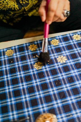 Close-up of artisan hands applying gold leaf to a decorative piece in a workshop.