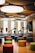 A modern music room with various drums and musical instruments set on a stage. The space features colorful, round seating stools scattered across a wooden floor, and circular acoustic panels hanging from the ceiling. Natural light filters through large windows in the background.