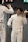 Two fencers in white protective gear are in a duel. One fencer is holding a foil and removing his mask, while the other fencer, also holding a foil, is partially visible. The background shows a digital scoreboard and an exit sign.
