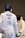 Two fencers are engaged in a bout. The foreground fencer, seen from behind, wears protective gear with a white jacket displaying 'BALKA SUI' and other logos. The fencer in the background faces forward with an obscured face due to their mask. Both are poised with their foils.