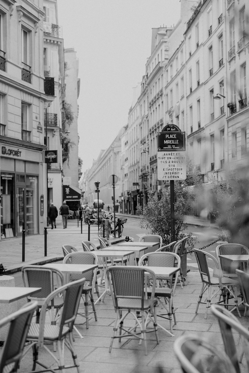 a black and white photo of tables and chairs on a sidewalk