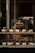 A bakery display window featuring an assortment of pastries and bread. The shelves are lined with various baked goods like croissants, muffins, and loaves, each accompanied by small name cards. The display is warmly lit, creating a cozy and inviting atmosphere.