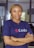 A person with braided hair is standing with their arms crossed, wearing a navy blue shirt with the word 'Codar' printed on it. The background appears to be an indoor setting, possibly an office.
