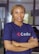 A person with braided hair is standing with their arms crossed, wearing a navy blue shirt with the word 'Codar' printed on it. The background appears to be an indoor setting, possibly an office.