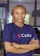 A person with braided hair is standing with their arms crossed, wearing a navy blue shirt with the word 'Codar' printed on it. The background appears to be an indoor setting, possibly an office.