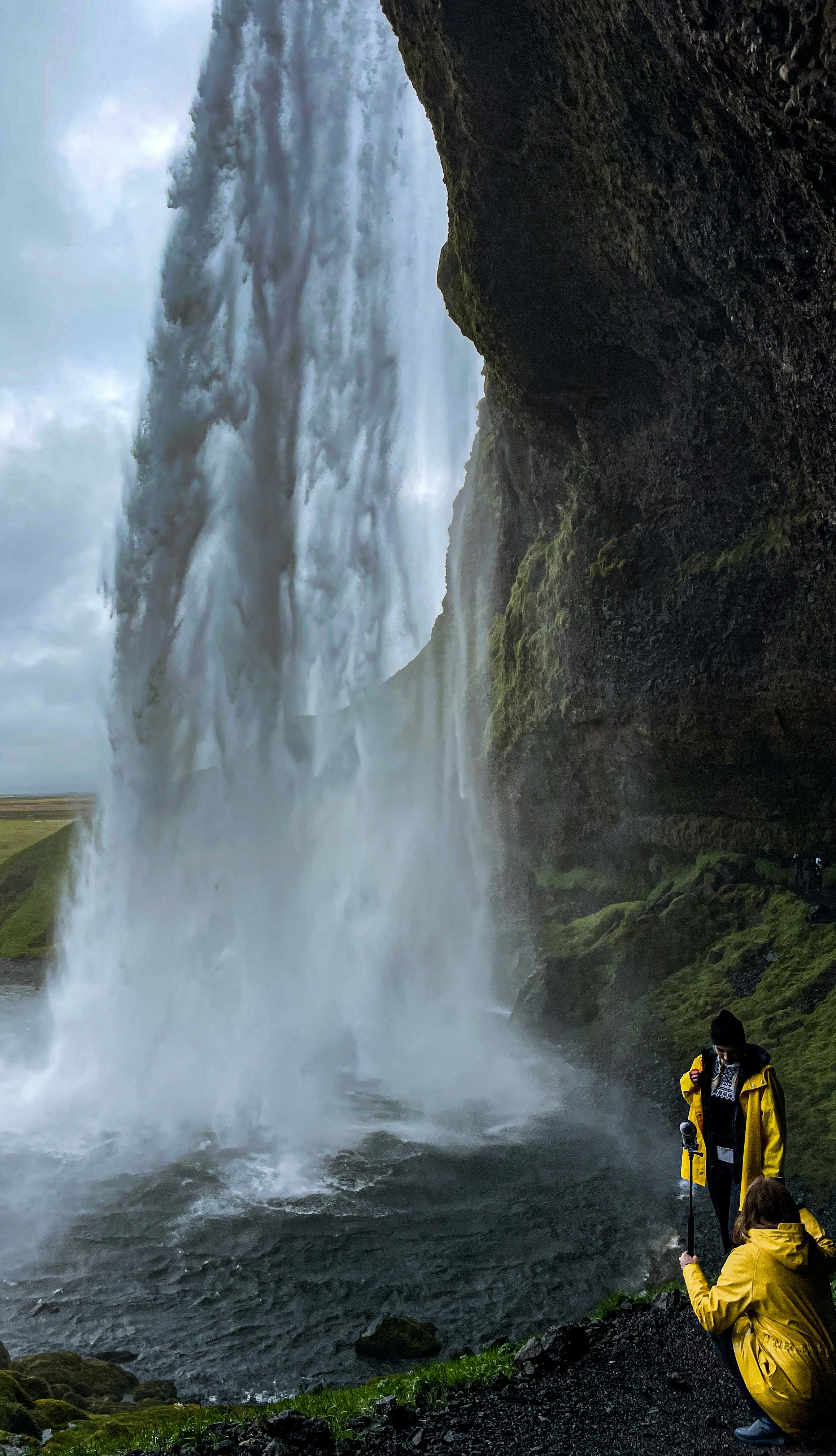 Ein Mann in einer gelben Jacke, der vor einem Wasserfall steht