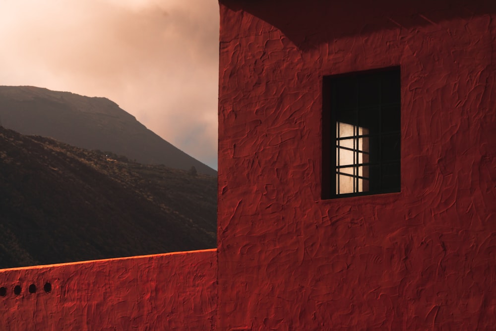 a red building with a window and a mountain in the background