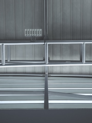 Metallic beams and supports form a structured pattern against a ribbed industrial ceiling. Several rectangular vents or panels are visible, adding to the utilitarian design.