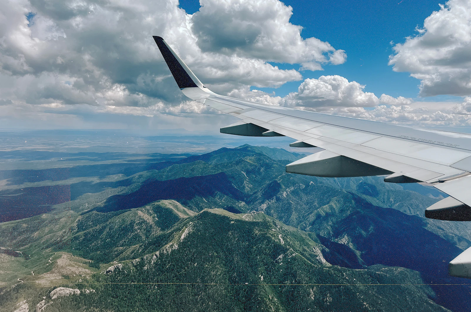 山脈の上を飛ぶ飛行機の翼を窓越しに見た写真。海外旅行と年代の話を象徴するイメージ