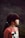 A young girl with dark hair tied in a ponytail is seen in profile view against a blurry outdoor background. She is wearing a reddish-brown shirt featuring a graphic of a cat with a bow.