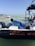 A person wearing a blue shirt is working on a small black and white boat on the water, with the text 'Soc. Coop. Ensueño del Caribe SCL' visible. In the background, another boat with several seated people wearing life vests is seen. The sky is clear and the water is calm.