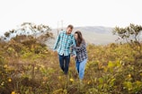 A couple laughing and holding hands while walking through a field of wildflowers.