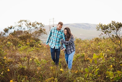 A couple laughing and holding hands while walking through a field of wildflowers.