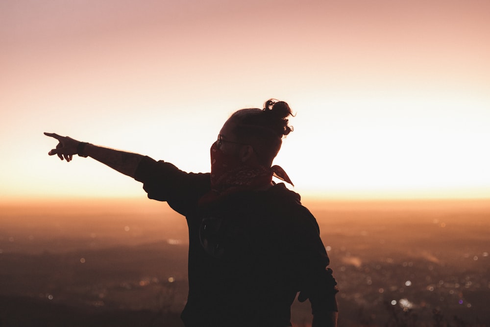 a person pointing at the sky with a sunset in the background