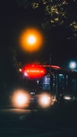 A bus is illuminated against the night sky, with its headlights on and a bright, glowing sign displaying '82 Carnival'. The surrounding area is dark, with a streetlight casting a warm, orange glow.