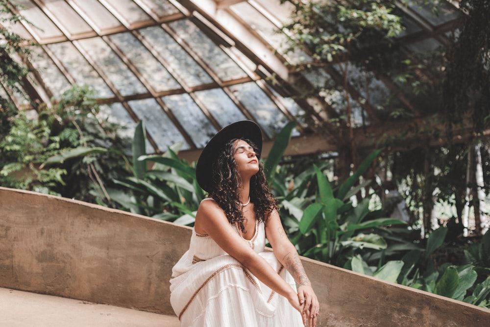 a woman sitting on a ledge in a greenhouse