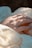 A close-up of a hand adorned with a gold ring featuring a square gemstone resting gently. The surrounding fabric appears to be delicate and embroidered, creating an elegant and serene atmosphere.