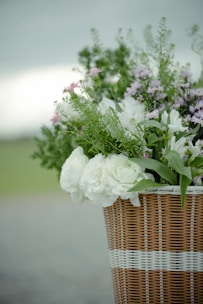 A vibrant bouquet of mixed seasonal flowers in soft pastel tones, arranged in a rustic wicker basket.