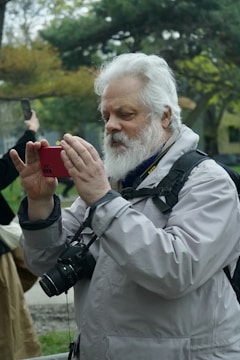 An elderly person using a smartphone to take pictures outdoors.