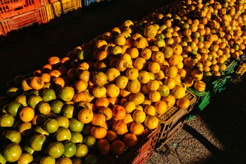 A large assortment of fruits, mainly oranges and limes, is displayed in plastic crates. The fruits are organized in neat rows, with oranges predominantly on the right and limes on the left. The crates add a variety of color to the scene, creating a warm and inviting market atmosphere.