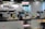 A modern office space with rows of desks, each equipped with computer monitors and office chairs. There are Indian flags hanging from the ceiling. The desks have various items on them, including sticky notes, water bottles, and some personal items. Plants are hanging from the ceiling, adding a touch of greenery. The word 'swipe' is displayed on the wall.