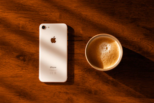 A sleek smartphone resting on a wooden table beside a cup of coffee, bathed in soft morning light.