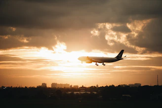 Elegant airplane soaring above clouds during golden hour with a hint of city skyline below.