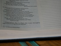 An open book displaying text from a religious scripture with passages discussing prophets and their actions. The text is printed on a page with a slightly yellowed and aged appearance.