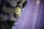 A close-up of an elegantly arranged floral decoration featuring white and pale purple roses intertwined with green leaves. The delicate flowers are adorned with small fairy lights, and the background fades into soft hues of lavender.