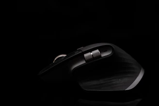 A sleek, dark ergonomic computer mouse with a metallic scrolling wheel, illuminated against a black background, showcasing its curved design and textured grip.
