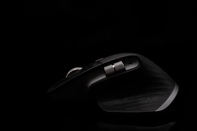 A sleek, dark ergonomic computer mouse with a metallic scrolling wheel, illuminated against a black background, showcasing its curved design and textured grip.
