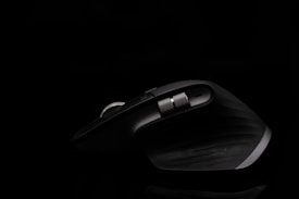 A sleek, dark ergonomic computer mouse with a metallic scrolling wheel, illuminated against a black background, showcasing its curved design and textured grip.