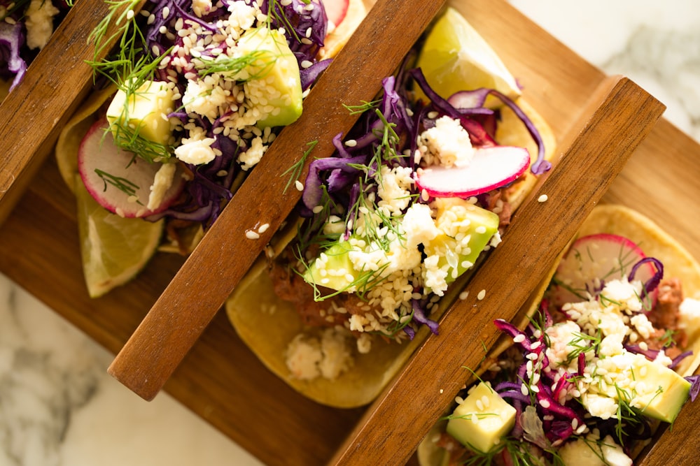 a wooden tray topped with three tacos covered in veggies