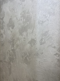 A textured wall with a plaster-like appearance, featuring a mix of light gray and subtle warm tones. The surface displays a variety of brushstroke patterns, creating a rustic and uneven visual effect.