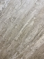 A textured surface with a rough, naturalistic pattern that resembles stone or concrete. The surface features various shades of gray with patches of lighter and darker areas, creating a rugged, layered effect.