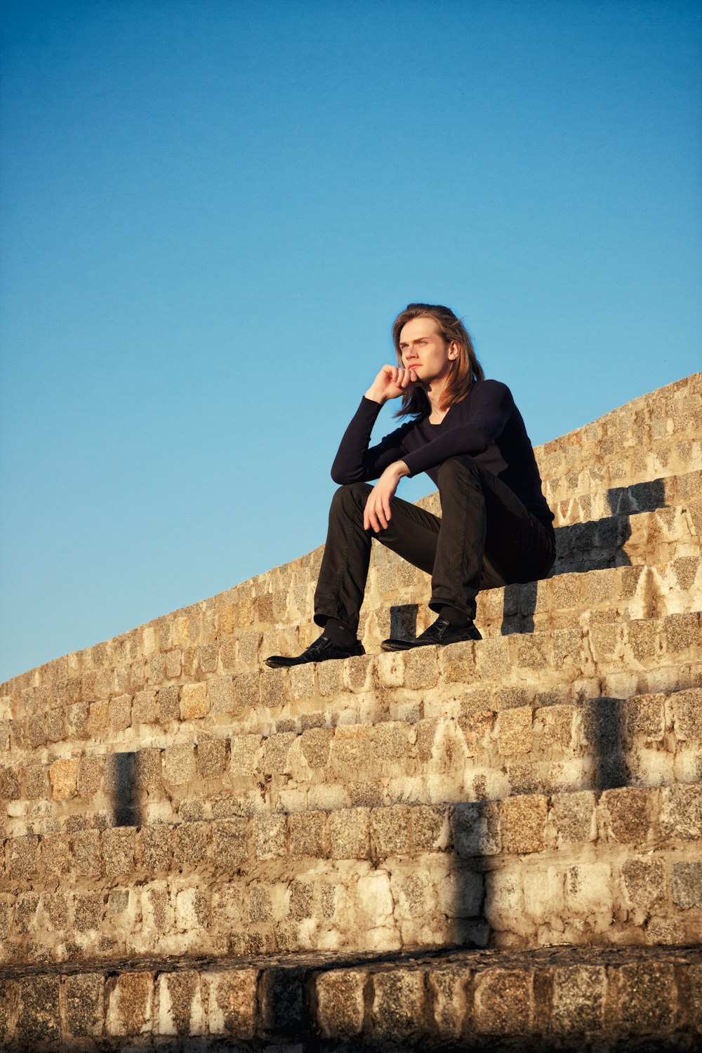 a woman is sitting on a stone wall