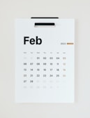 A minimalist wall calendar displays the month of February 2023, with days of the week arranged in a grid. The numbers are printed in black except for the Sundays, which are in brown.
