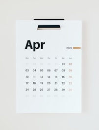 A wall calendar displaying the month of April 2023 with dates arranged in a grid format. The days of the week are listed at the top, and the numbers of the days are printed below in bold black and muted gold colors. The background is a clean, minimalist white, and the page is held by a black clip at the top.
