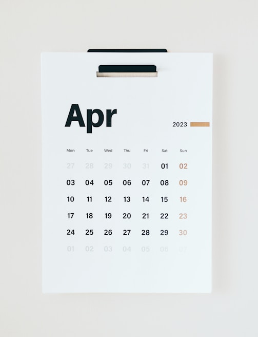 A wall calendar displaying the month of April 2023 with dates arranged in a grid format. The days of the week are listed at the top, and the numbers of the days are printed below in bold black and muted gold colors. The background is a clean, minimalist white, and the page is held by a black clip at the top.
