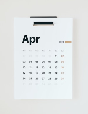 A wall calendar displaying the month of April 2023 with dates arranged in a grid format. The days of the week are listed at the top, and the numbers of the days are printed below in bold black and muted gold colors. The background is a clean, minimalist white, and the page is held by a black clip at the top.