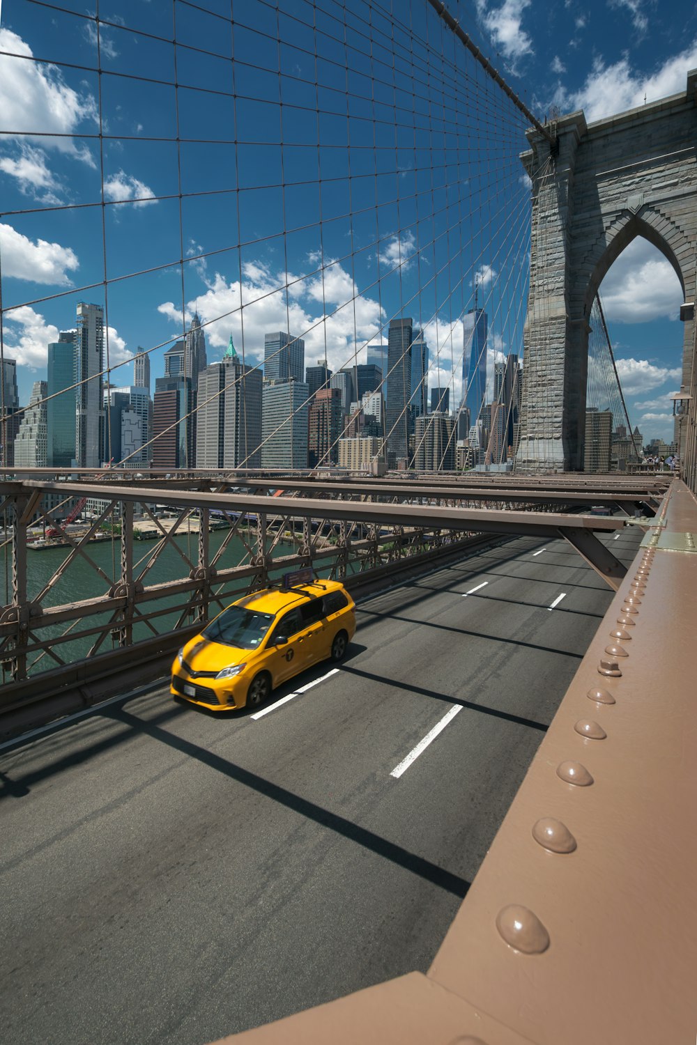 a yellow car driving across a bridge over water