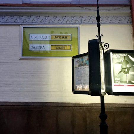 The image features a vintage-style signpost in front of a building with decorative molding. A yellow and white sign on the wall highlights upcoming events, listing a performance of 'The Nutcracker' for today and a concert for tomorrow. Another part of the signpost displays posters with text and images, including a dancer in mid-movement.