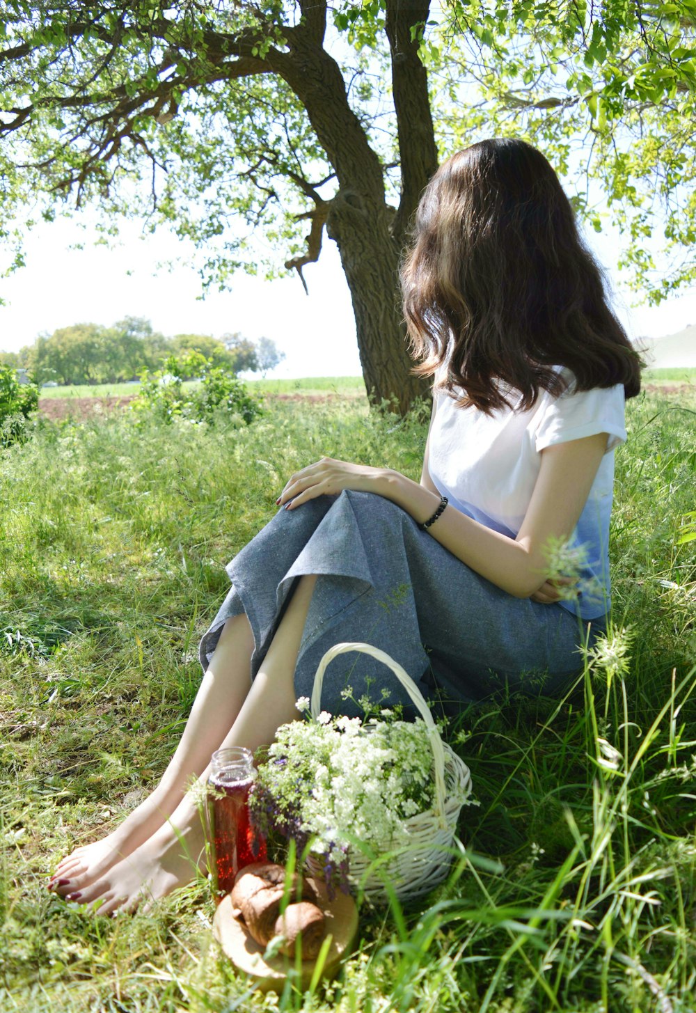 a woman sitting in the grass next to a tree