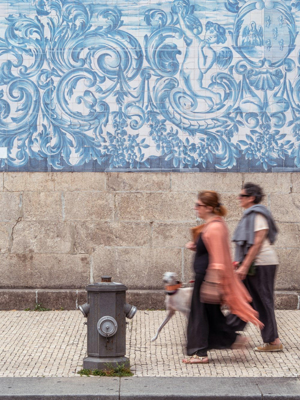 two people walking down a sidewalk next to a fire hydrant