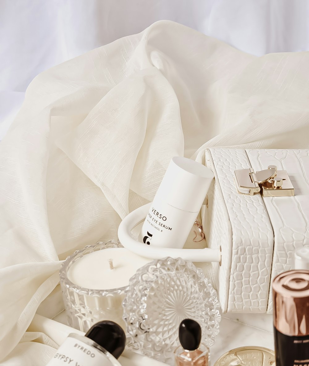 a white purse sitting on top of a bed next to bottles of perfume