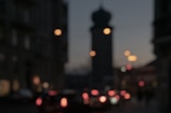A city street at dusk with glowing street lamps and blurred passing cars.