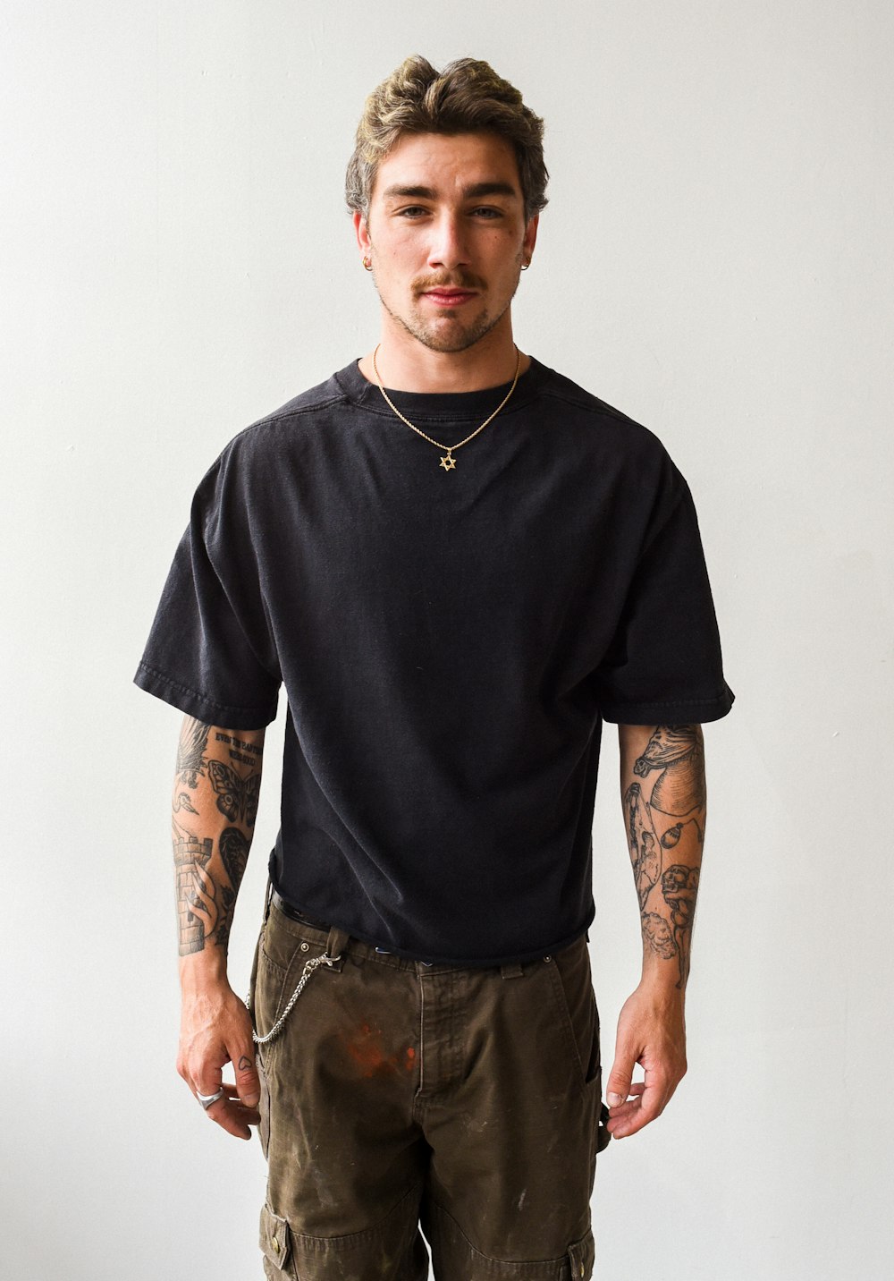 a man with tattoos standing in front of a white wall