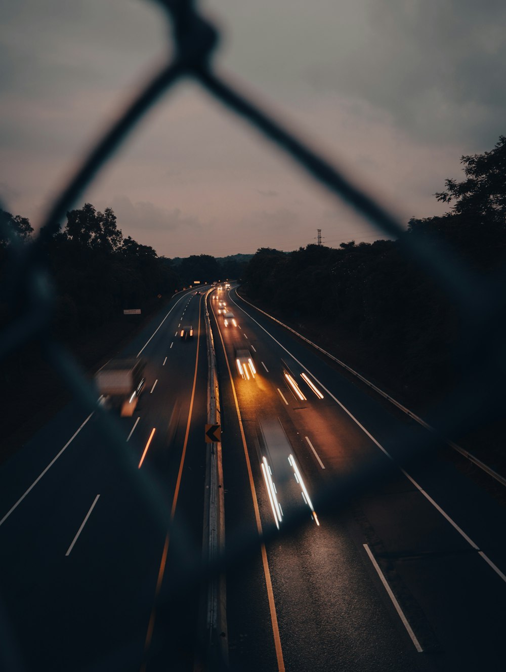 a view of a highway at night through a chain link fence