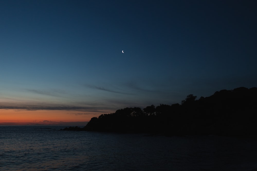 the sun is setting over the ocean with a small island in the foreground