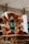 A basket filled with artisan bread, featuring a large, uniquely shaped loaf with an abstract design placed prominently. The background includes softly blurred interior lights and shelves with various items, creating a cozy atmosphere.